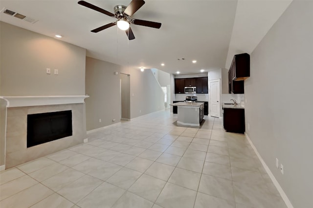 unfurnished living room with sink, a tile fireplace, ceiling fan, and light tile patterned flooring