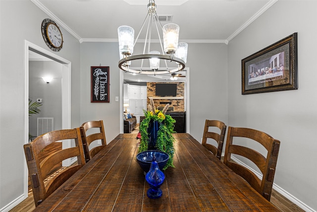 dining area featuring crown molding, a stone fireplace, dark wood-type flooring, and ceiling fan with notable chandelier