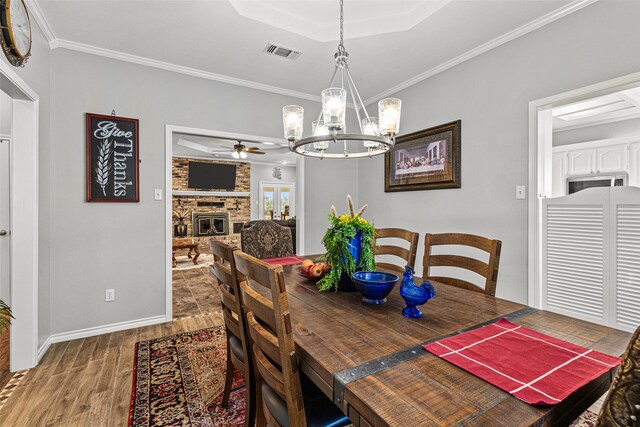 dining area with ceiling fan with notable chandelier, a fireplace, wood-type flooring, ornamental molding, and a tray ceiling