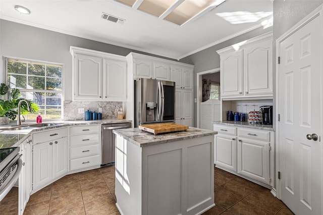 kitchen featuring a kitchen island, white cabinetry, sink, backsplash, and stainless steel appliances