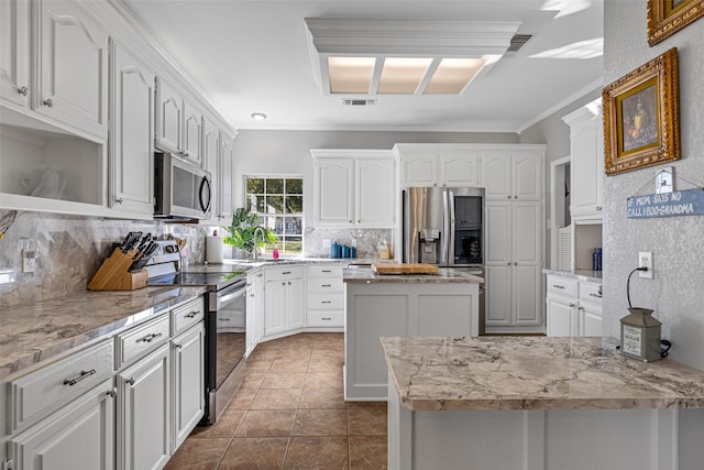 kitchen with crown molding, white cabinetry, stainless steel appliances, light stone countertops, and a kitchen island