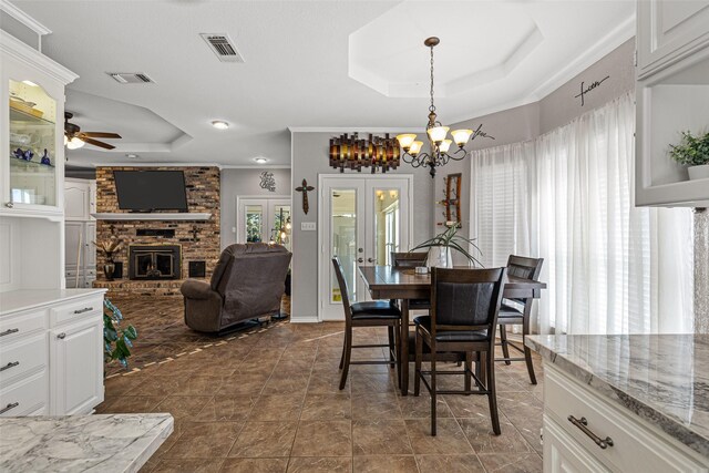 dining area featuring crown molding, a tray ceiling, a brick fireplace, ceiling fan with notable chandelier, and french doors