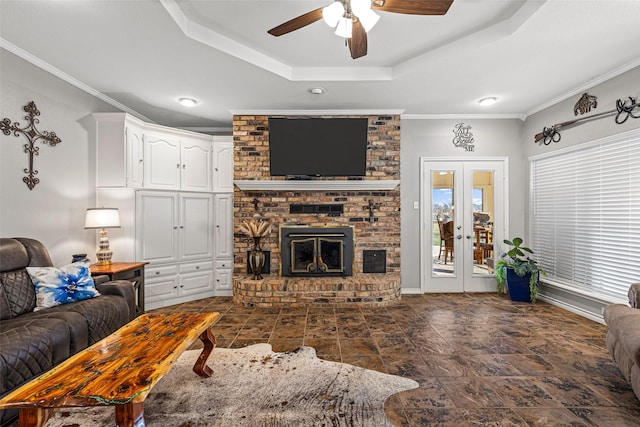 living room with crown molding, plenty of natural light, a tray ceiling, a brick fireplace, and french doors