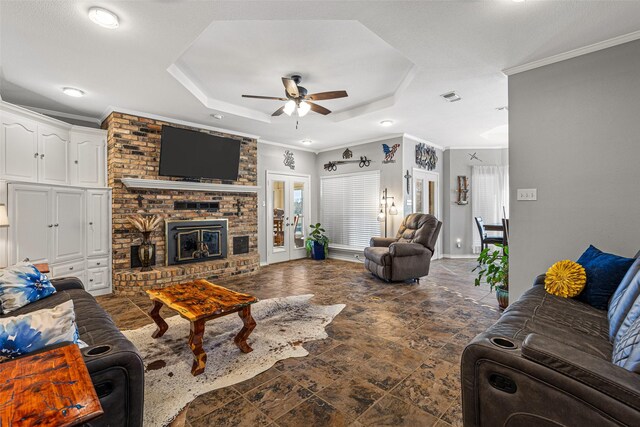 living room featuring ceiling fan, ornamental molding, a fireplace, and a raised ceiling