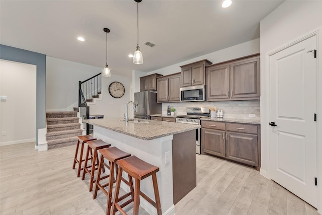 kitchen with light hardwood / wood-style flooring, a kitchen island with sink, stainless steel appliances, a kitchen breakfast bar, and light stone counters