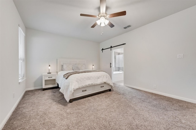 carpeted bedroom featuring multiple windows, a barn door, ceiling fan, and ensuite bathroom