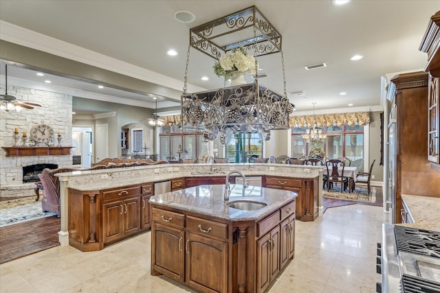 kitchen with a spacious island, sink, pendant lighting, a fireplace, and ceiling fan with notable chandelier