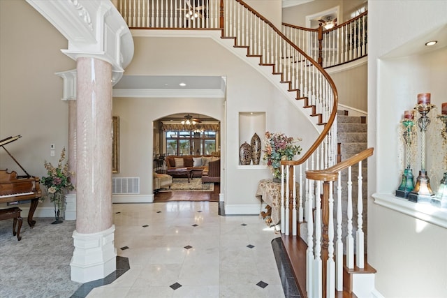 foyer featuring ornate columns, ornamental molding, a towering ceiling, and ceiling fan