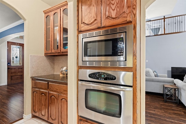 kitchen with appliances with stainless steel finishes, dark hardwood / wood-style floors, tasteful backsplash, dark stone counters, and crown molding