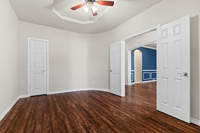 empty room featuring dark wood-type flooring, ceiling fan, and a tray ceiling