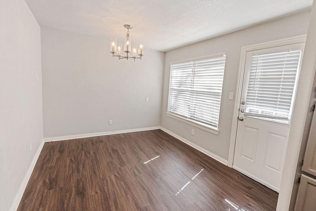 unfurnished dining area with a chandelier, dark wood finished floors, and baseboards