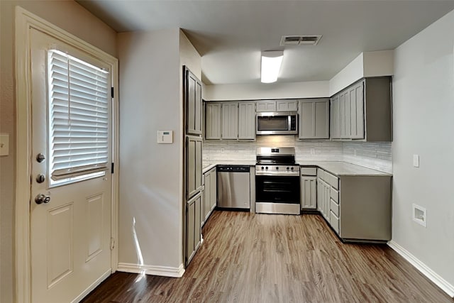 kitchen with light wood-type flooring, decorative backsplash, gray cabinets, and appliances with stainless steel finishes