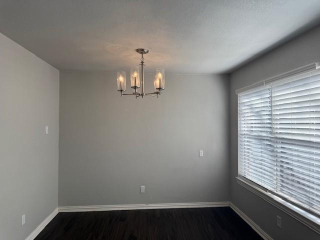 unfurnished room featuring dark wood-type flooring and a notable chandelier