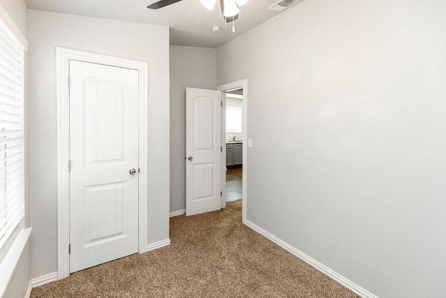 unfurnished bedroom with carpet flooring, baseboards, multiple windows, and a ceiling fan