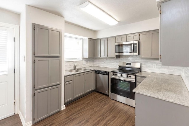 kitchen featuring stainless steel appliances, gray cabinets, a sink, dark wood-style flooring, and tasteful backsplash