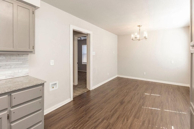 unfurnished dining area with a chandelier, dark wood-style floors, and baseboards