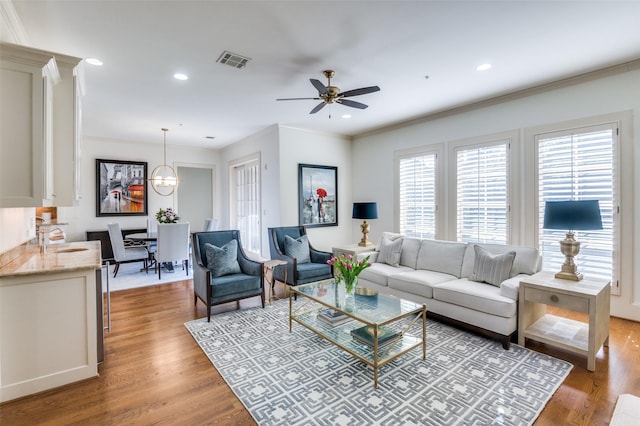 living room with crown molding, sink, ceiling fan with notable chandelier, and light hardwood / wood-style floors