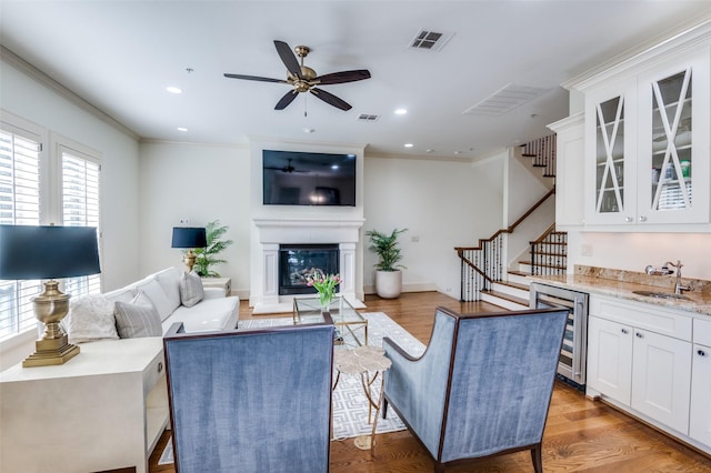 living room featuring crown molding, indoor wet bar, wine cooler, and light hardwood / wood-style flooring