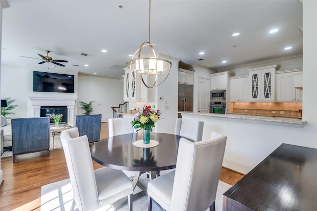 dining space with ceiling fan with notable chandelier, light hardwood / wood-style flooring, and ornamental molding