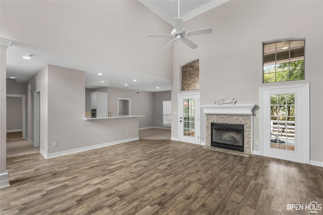 unfurnished living room featuring crown molding, a towering ceiling, wood-type flooring, and ceiling fan