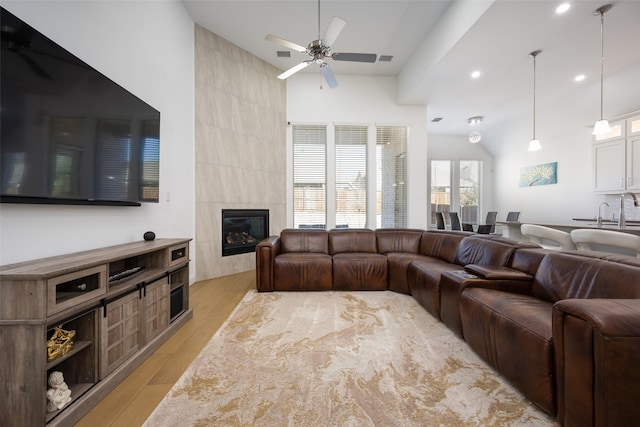 living room with lofted ceiling, a fireplace, ceiling fan, and light wood-type flooring