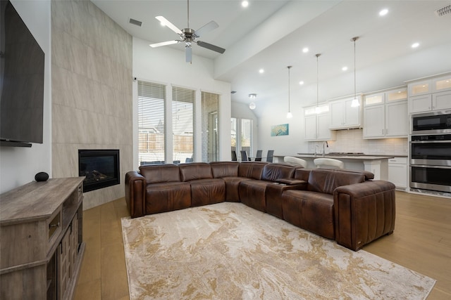 living room with ceiling fan, a tile fireplace, and light wood-type flooring