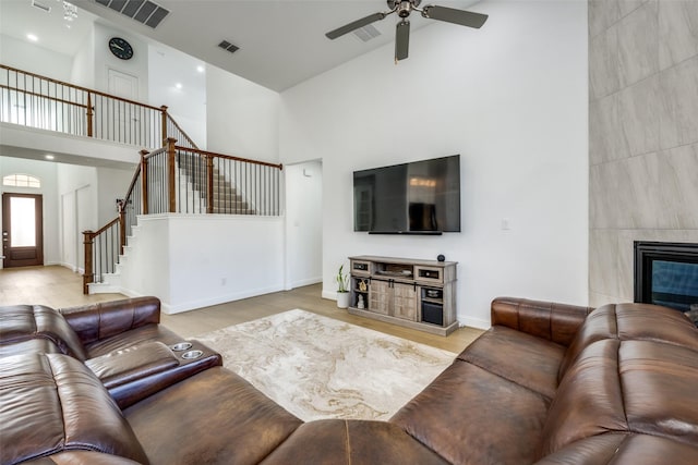 living room with ceiling fan, a tiled fireplace, high vaulted ceiling, and light wood-type flooring