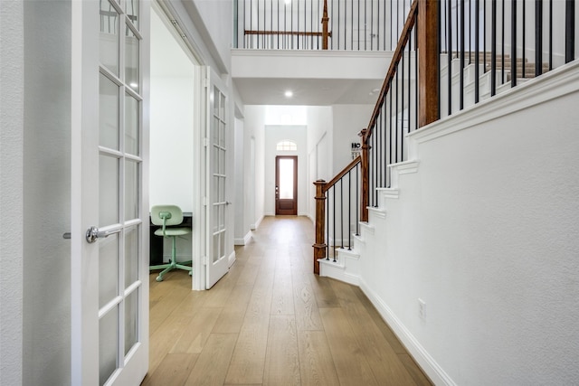 entryway with a high ceiling, light hardwood / wood-style flooring, and french doors