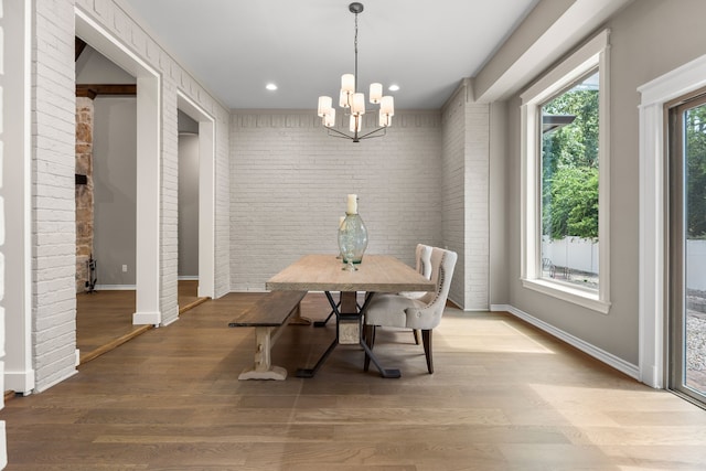 dining room featuring hardwood / wood-style flooring, brick wall, and a chandelier