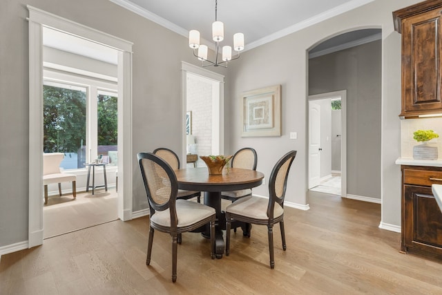 dining space with ornamental molding, an inviting chandelier, and light hardwood / wood-style flooring