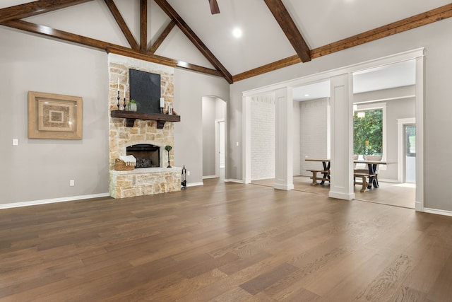 living room featuring hardwood / wood-style flooring, a stone fireplace, high vaulted ceiling, and beam ceiling