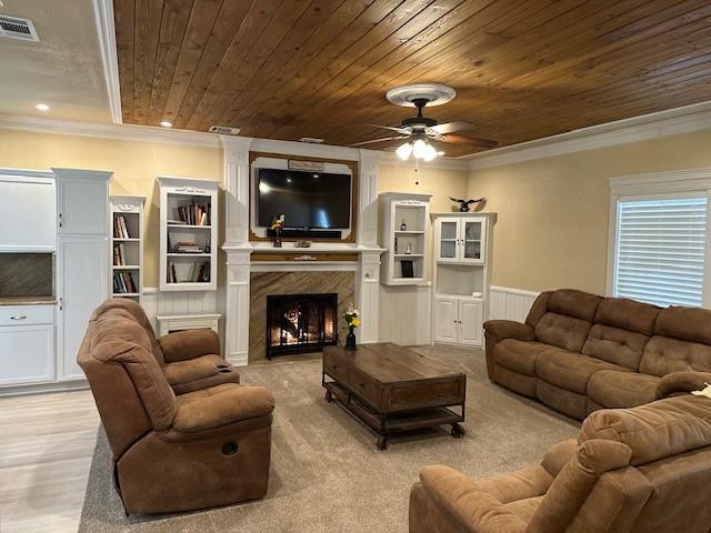 living room featuring wood ceiling, ornamental molding, a premium fireplace, and ceiling fan