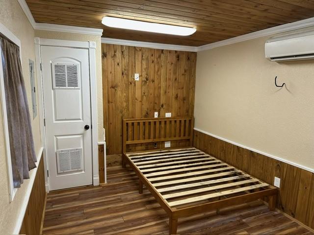 interior space featuring wooden walls, ornamental molding, dark wood-type flooring, wooden ceiling, and a wall unit AC