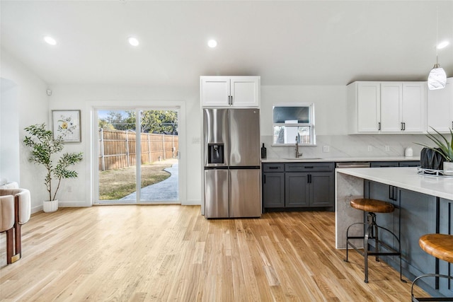 kitchen featuring a sink, a kitchen breakfast bar, stainless steel fridge with ice dispenser, light wood finished floors, and decorative backsplash