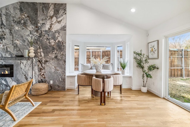 living area with vaulted ceiling, a tiled fireplace, and light hardwood / wood-style floors