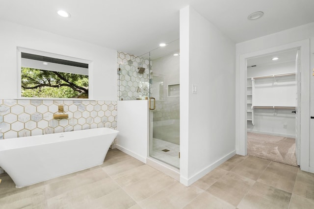 full bath with a walk in closet, recessed lighting, a stall shower, a soaking tub, and tile walls