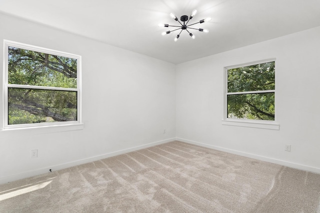 spare room featuring an inviting chandelier, a healthy amount of sunlight, and carpet flooring