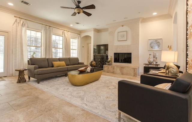 living room with a tiled fireplace, crown molding, and ceiling fan