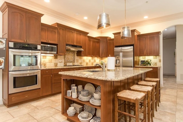 kitchen featuring appliances with stainless steel finishes, decorative light fixtures, sink, and a center island with sink