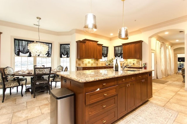 kitchen featuring pendant lighting, an island with sink, sink, decorative backsplash, and light stone counters