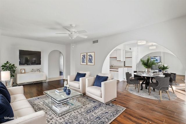 living area with a ceiling fan, visible vents, arched walkways, and dark wood finished floors