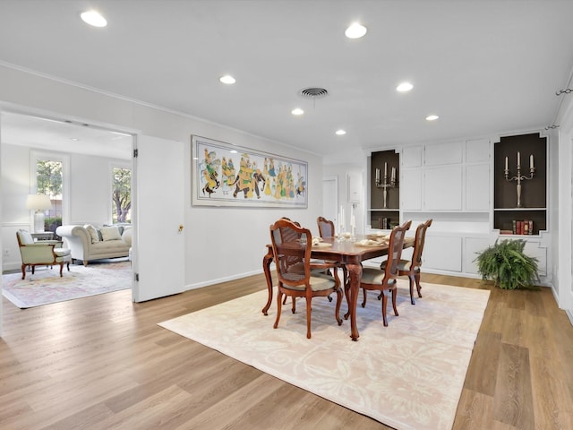 dining space with ornamental molding and light hardwood / wood-style flooring