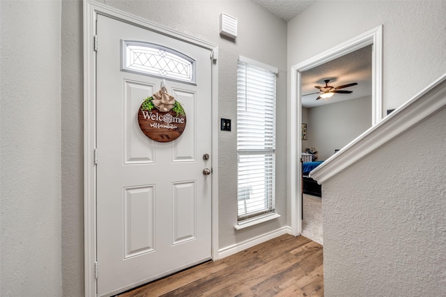 entryway featuring baseboards, a ceiling fan, a textured wall, wood finished floors, and a textured ceiling