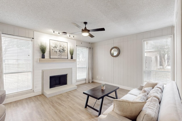 living room with light hardwood / wood-style flooring, rail lighting, ceiling fan, a textured ceiling, and a brick fireplace