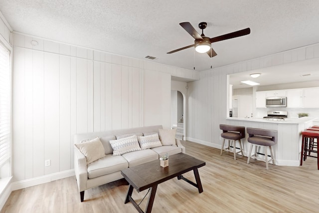 living room with ceiling fan, a textured ceiling, and light hardwood / wood-style flooring