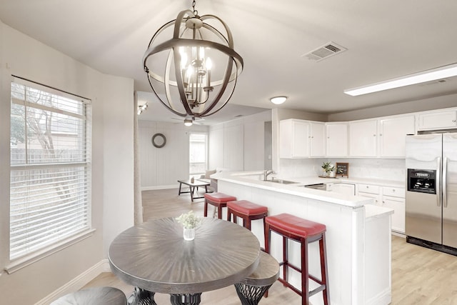 kitchen featuring stainless steel fridge with ice dispenser, white cabinetry, a kitchen breakfast bar, a chandelier, and kitchen peninsula