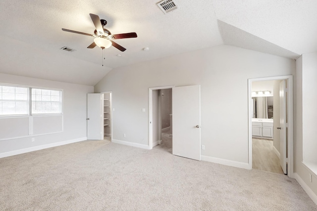 unfurnished bedroom with ensuite bathroom, lofted ceiling, a spacious closet, and ceiling fan