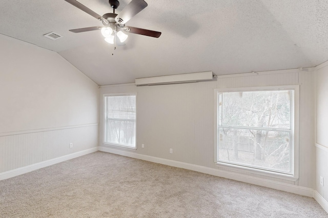 carpeted empty room featuring ceiling fan, vaulted ceiling, and a textured ceiling