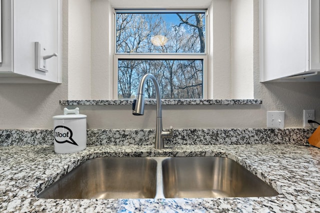 interior details featuring white cabinetry, sink, and light stone counters