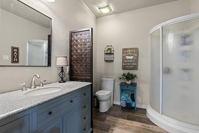 bathroom featuring toilet, a textured ceiling, vanity, a shower with door, and hardwood / wood-style floors